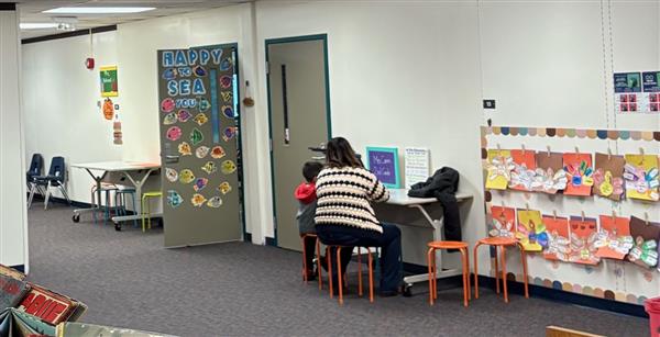 Teacher and student working at desk outside classroom. A wide shot of the walls and doors